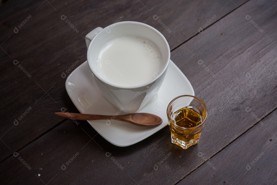Copo de leite com mel na mesa de madeira.