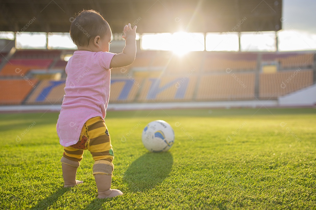 Bebê jogando futebol no estádio com pôr do sol.