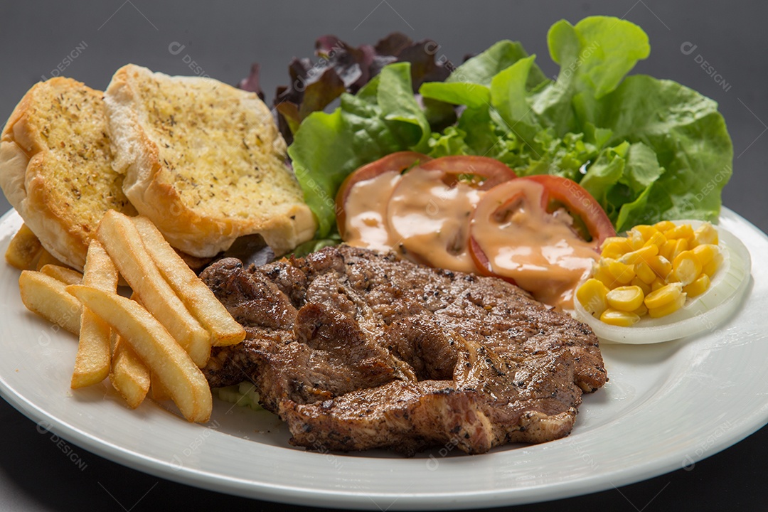 Prato branco de comida bife batata fritas com salada sobre uma mesa de restaurante