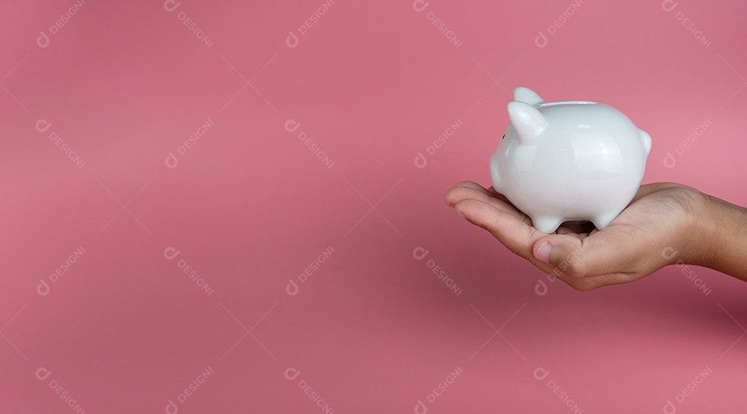 Uma mão humana segura o cofrinho branco. em um fundo rosa. Conceitos de poupança e investimento.