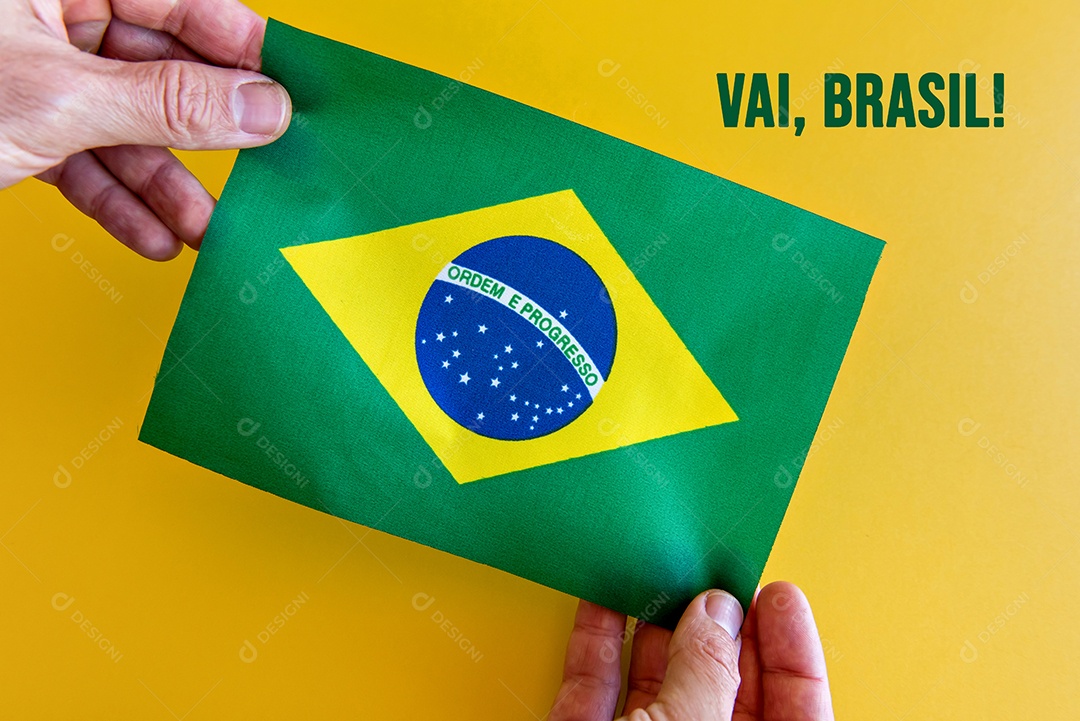 Hands holding the Brazilian flag on a yellow background