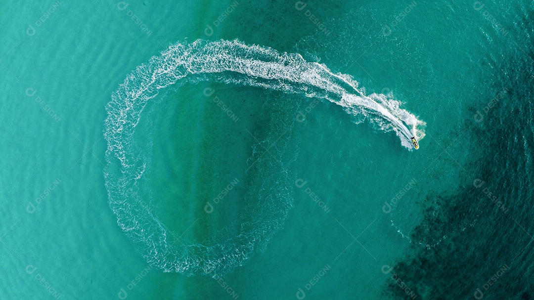 Tourist playing jet ski or scooter above fast water scooter in sea, riding in circle making beautiful white foam waves in clear pacific ocean. light turquoise on the tropical beach. top view action