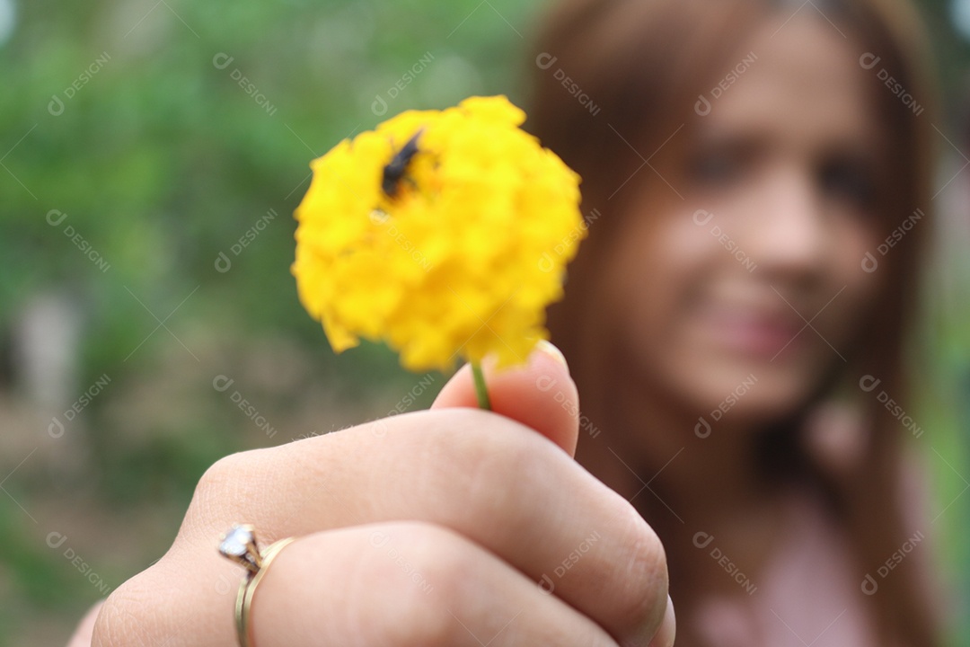 Mulher desfocada, segurando uma flor amarela com uma abelha