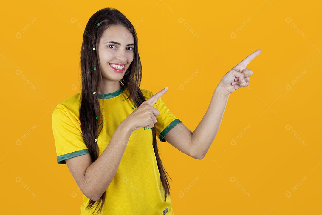 Linda mulher torcedora brasileira apontando para lado sobre fundo isolado amarelo