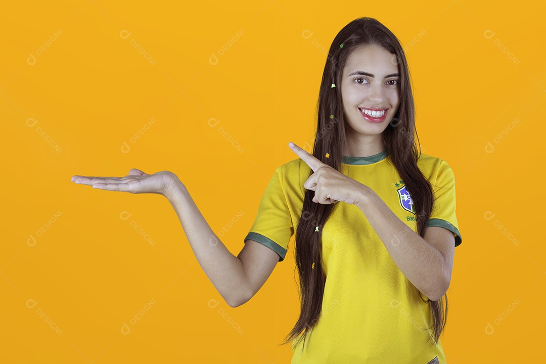 Linda mulher torcedora brasileira apontando para lado sobre fundo isolado amarelo