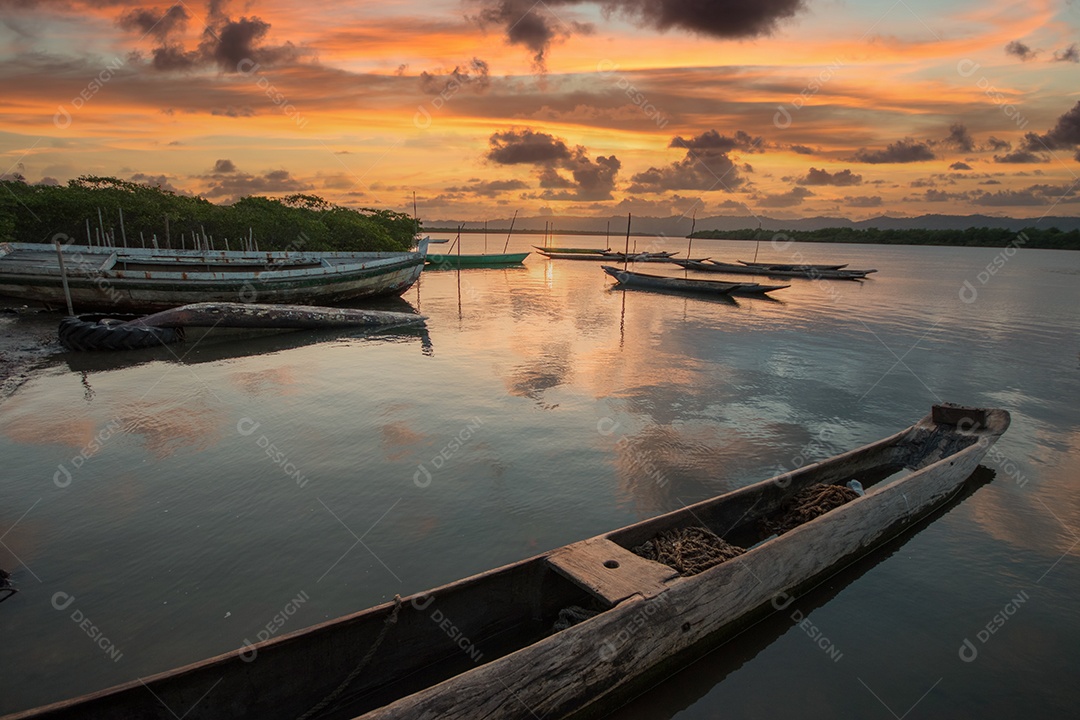 Paisagem com pôr do sol com canoas de pesca na beira do rio.