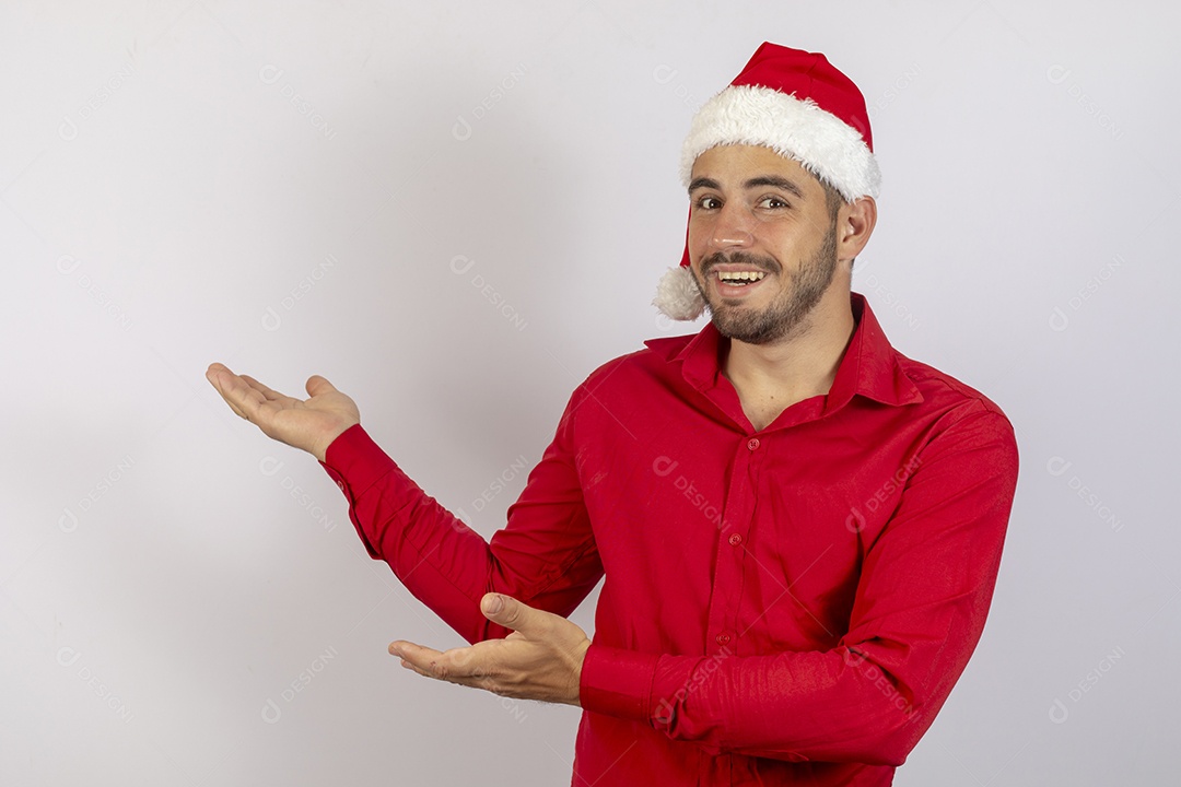 Homem jovem usando gorro Papai Noel apontando para lado sobre fundo branco