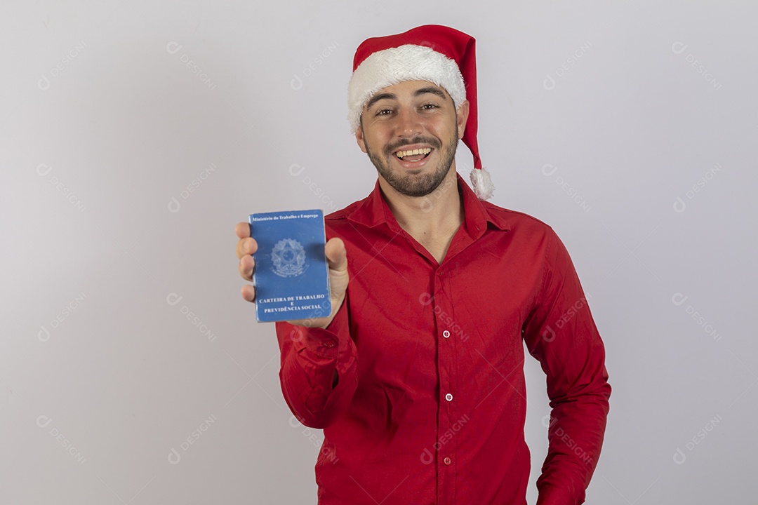 Homem jovem usando gorro Papai Noel segurando carteira de trabalho sobre fundo branco