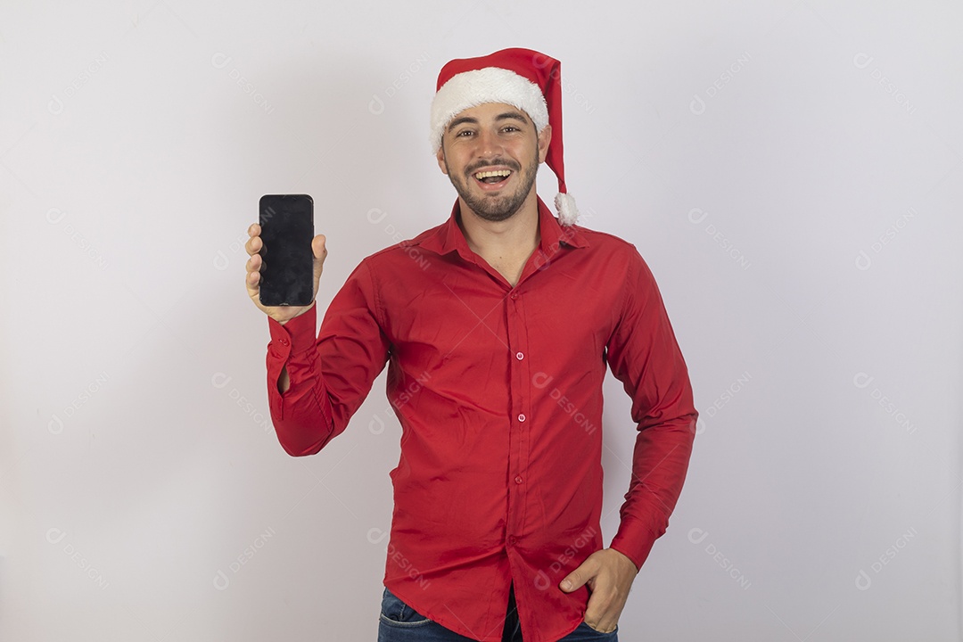 Homem jovem usando gorro Papai Noel segurando celular sobre fundo branco