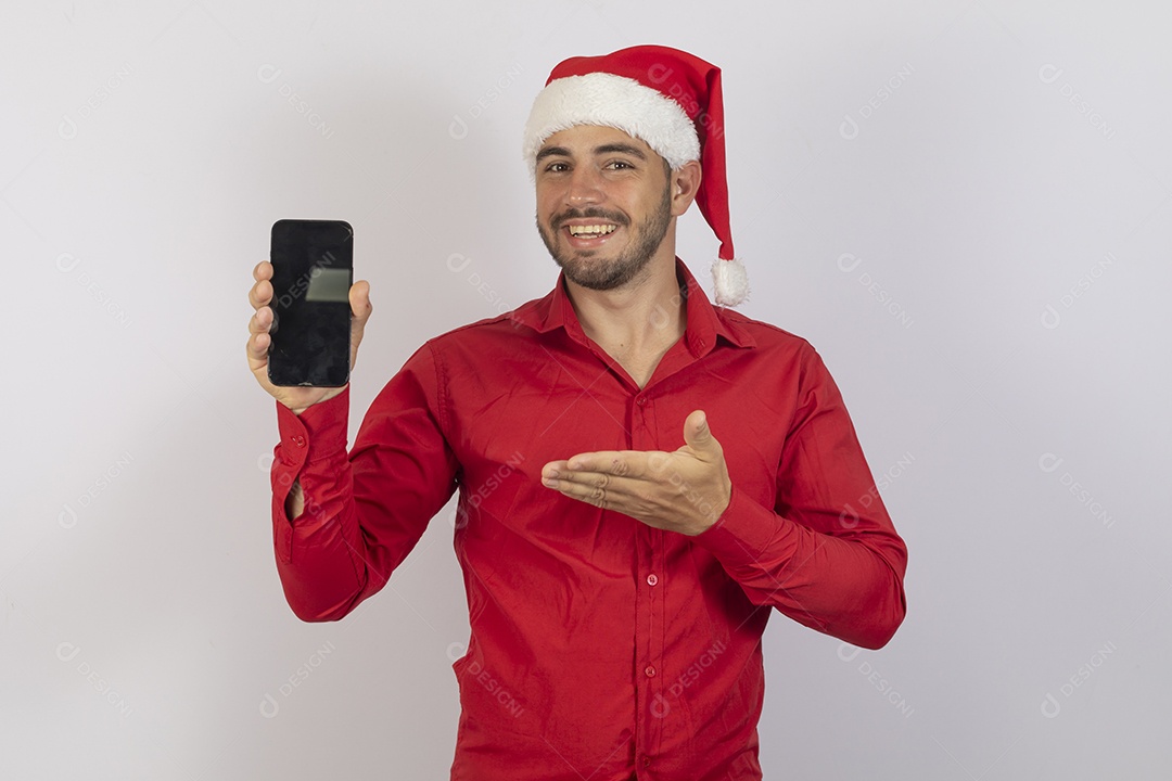 Homem jovem usando gorro Papai Noel segurando celular sobre fundo branco