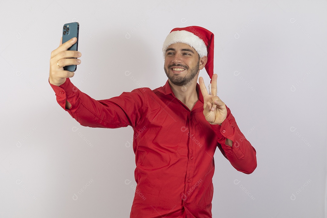 Homem jovem usando gorro Papai Noel segurando celular sobre fundo branco