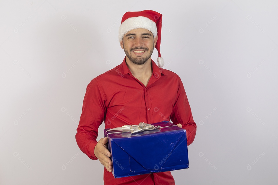 Homem jovem usando gorro Papai Noel segurando caixa de presente sobre fundo branco