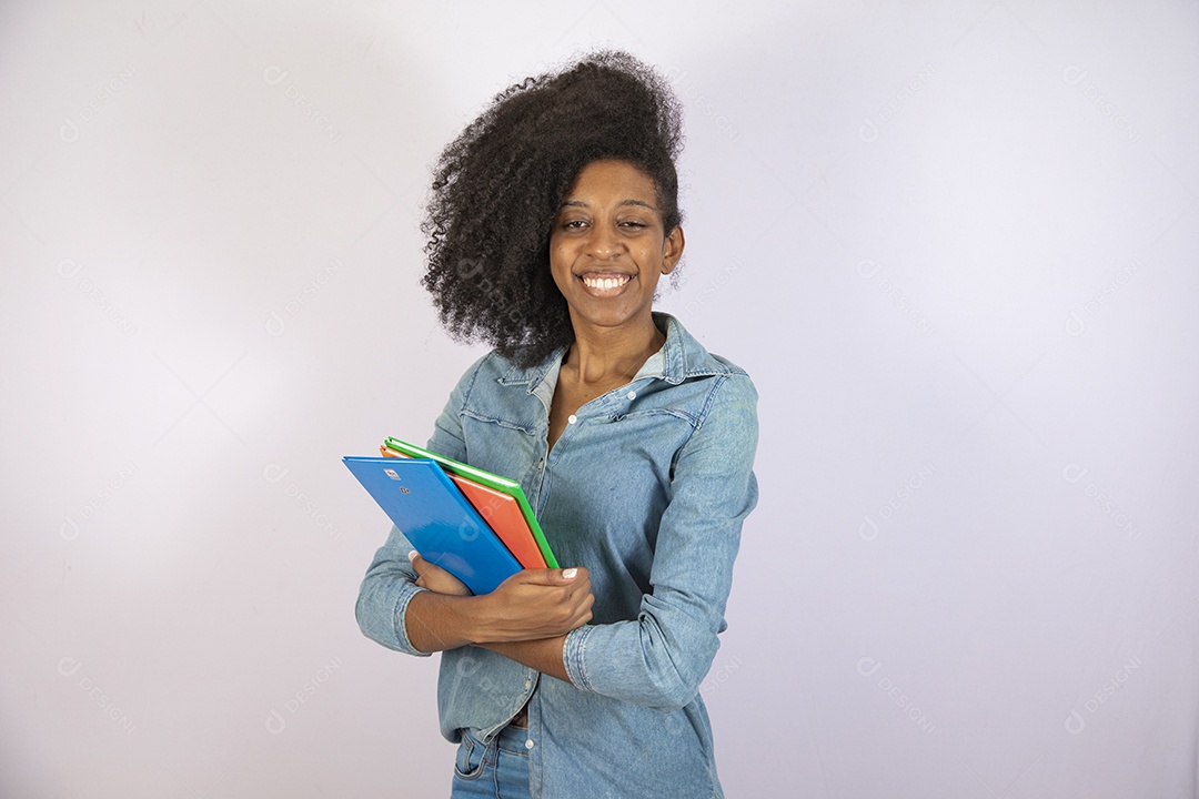 Mulher jovem negra cabelo cacheado segurando materiais escolar sobre fundo isolado branco