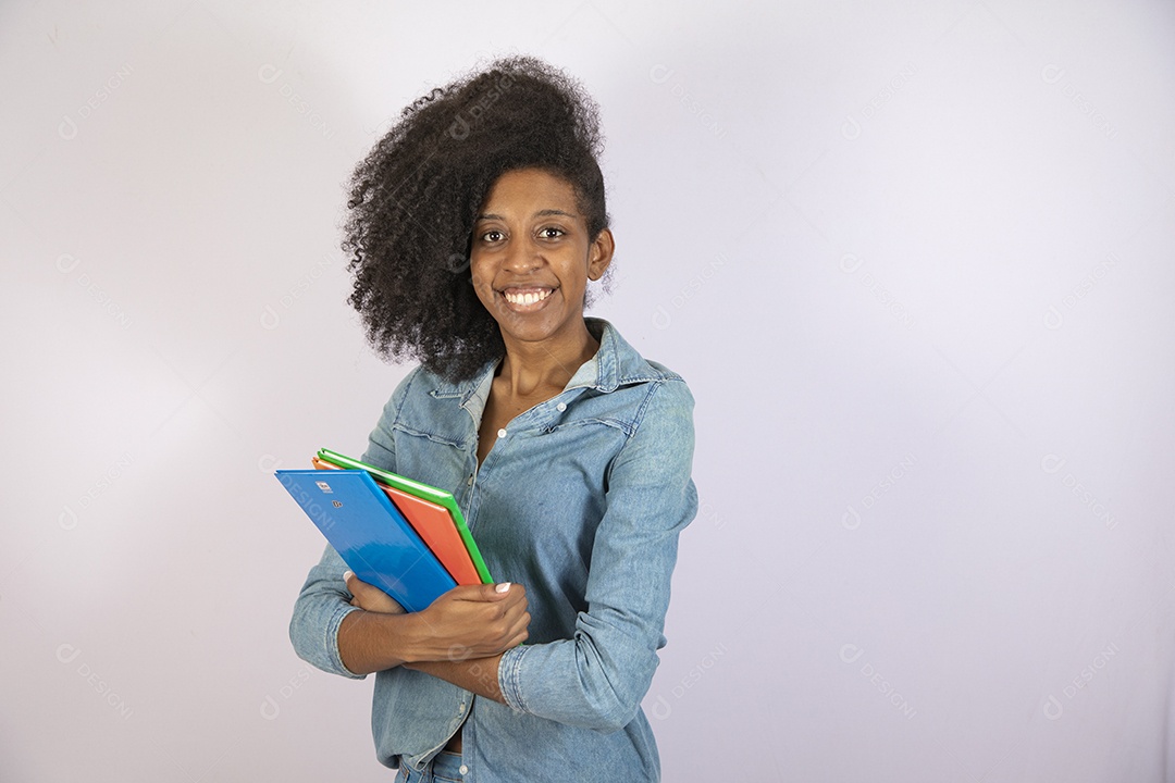 Mulher jovem negra cabelo cacheado segurando materiais escolar sobre fundo isolado branco