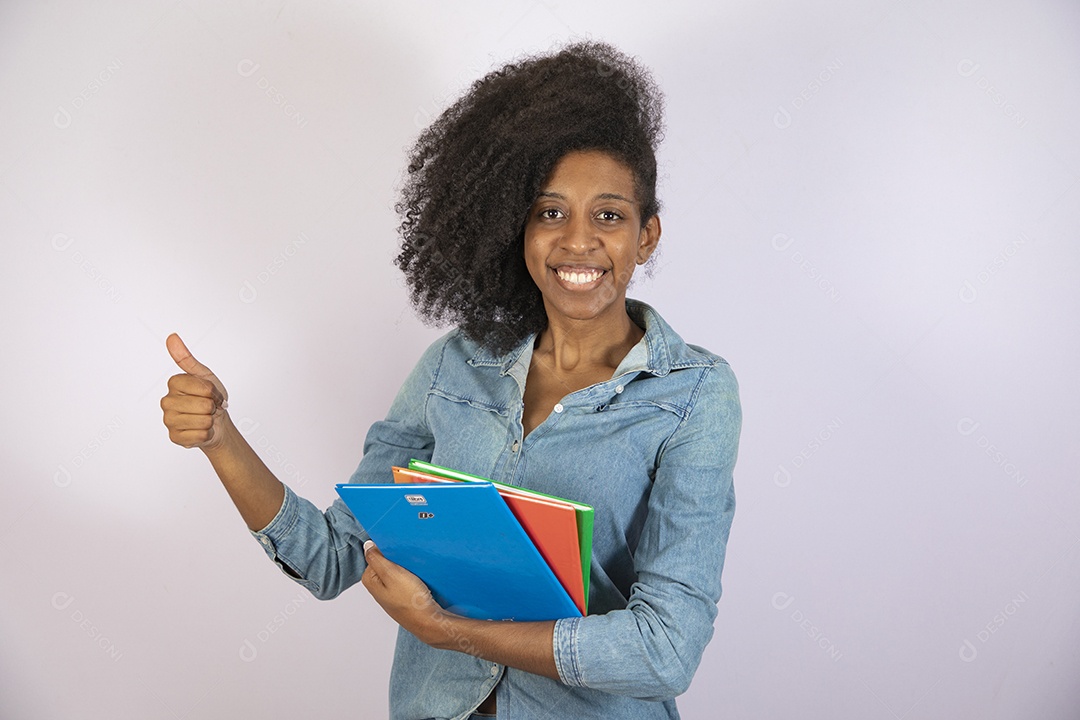 Mulher jovem negra cabelo cacheado segurando materiais escolar sobre fundo isolado branco