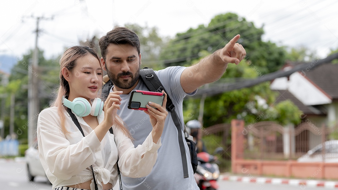 Jovem casal inter-racial viajando juntos, mulher asiática em busca de informações com smartphone, homem do Oriente Médio apontando para cima e olhando para smartphone, conceito de viagem.