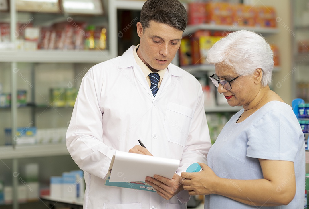 Um farmacêutico caucasiano aconselha uma idosa indiana a tratar doenças, recomendar medicamentos e fazer anotações.