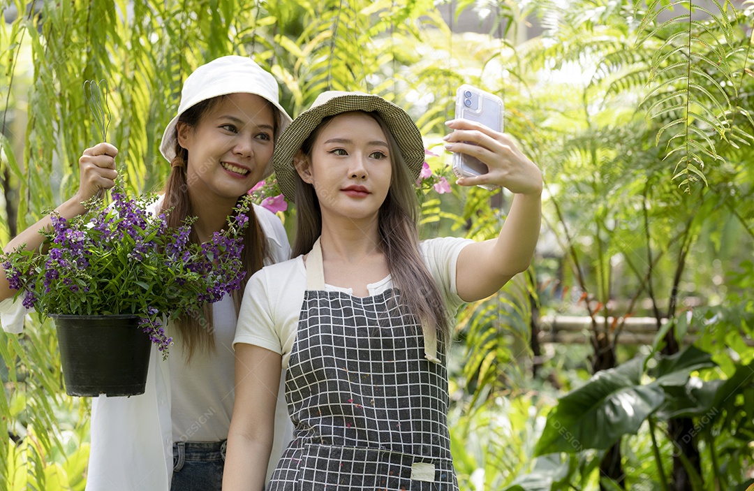 Duas lindas mulheres asiáticas usando smartphones para tirar selfies vendendo flores online, uma mulher na frente de uma selfie com um smartphone, uma mulher atrás segurando um vaso de flores, foto de meio corpo.