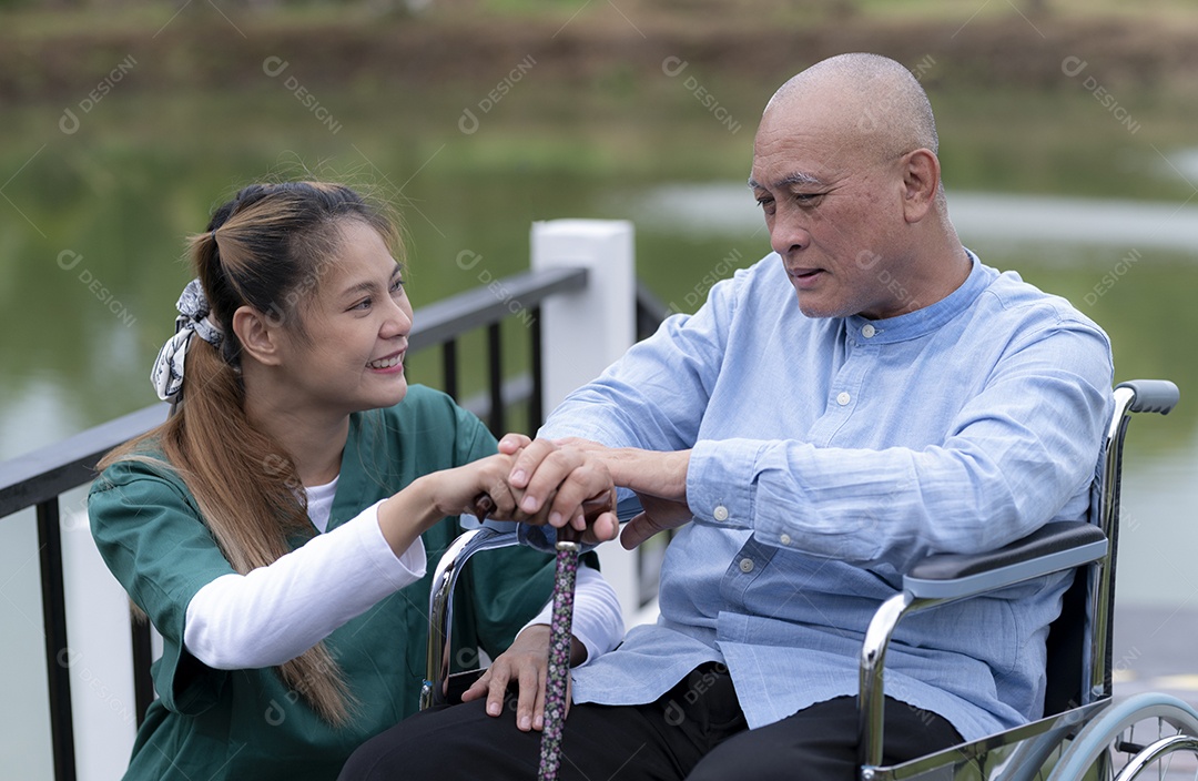 Uma mulher asiática fisioterapeuta em roupas verdes ajuda um homem idoso a se exercitar em uma cadeira de rodas em uma casa de repouso, cuidados de enfermagem.