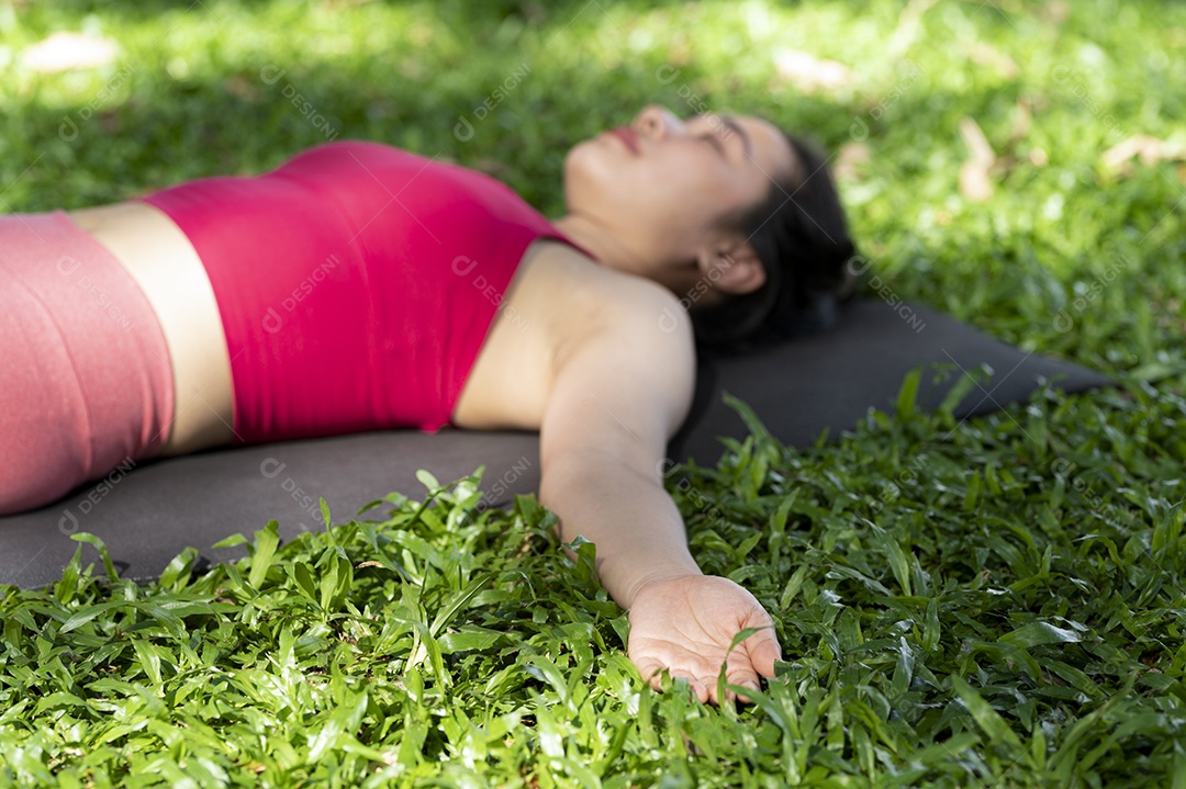 Mulher asiática fazendo poses de ioga para relaxamento muscular, ioga para meditação, exercitando-se no gramado ao ar livre.