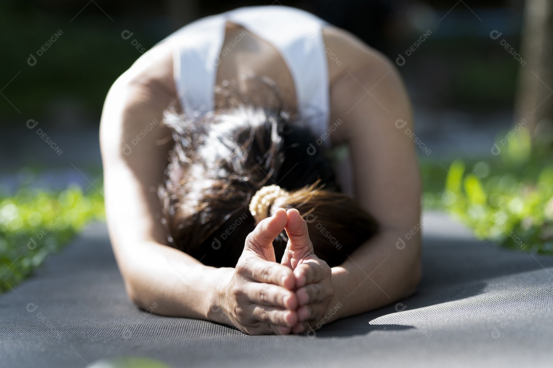 Mulher asiática fazendo poses de ioga para relaxamento muscular, ioga para meditação, exercitando-se no gramado ao ar livre.