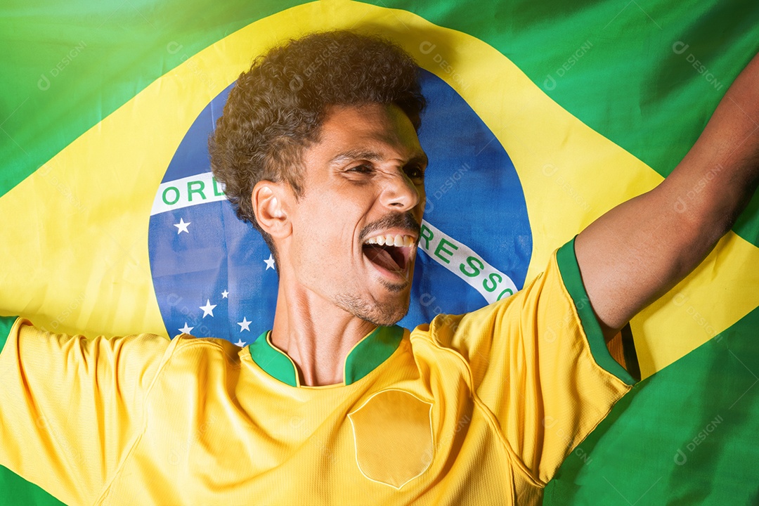 Fã de futebol brasileiro - homem negro segurando a bandeira do Brasil atrás comemorando