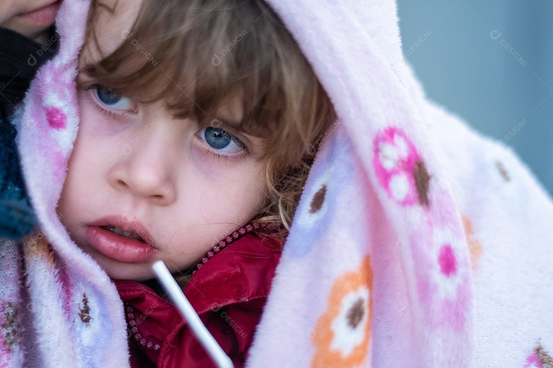 Linda garotinha nos braços da mãe, vestindo um cobertor na cabeça.