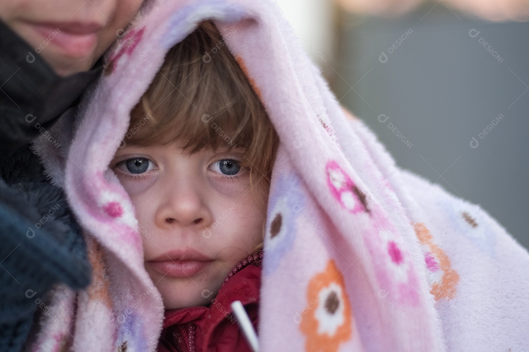 Linda garotinha nos braços da mãe, vestindo um cobertor na cabeça.
