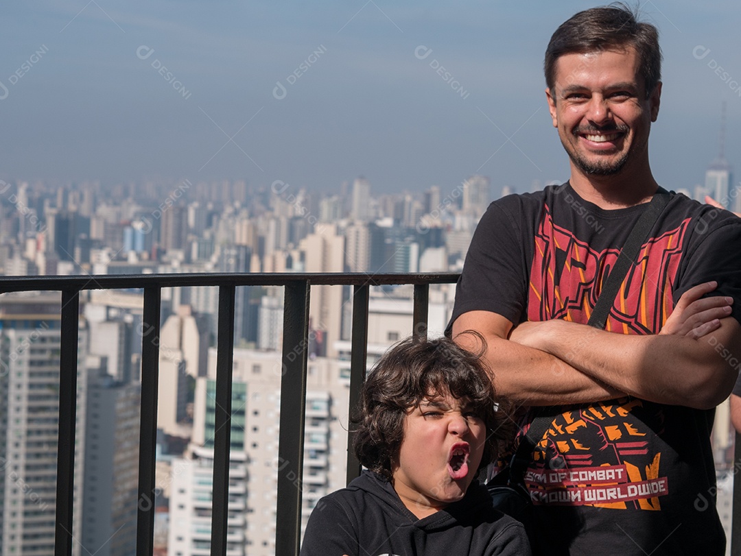 Pai e filho posando para a câmera em cima de um prédio no centro de São Paulo.