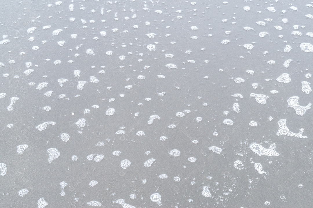 Superfície de praia de areia cinza ou escura com forma estranha de espuma