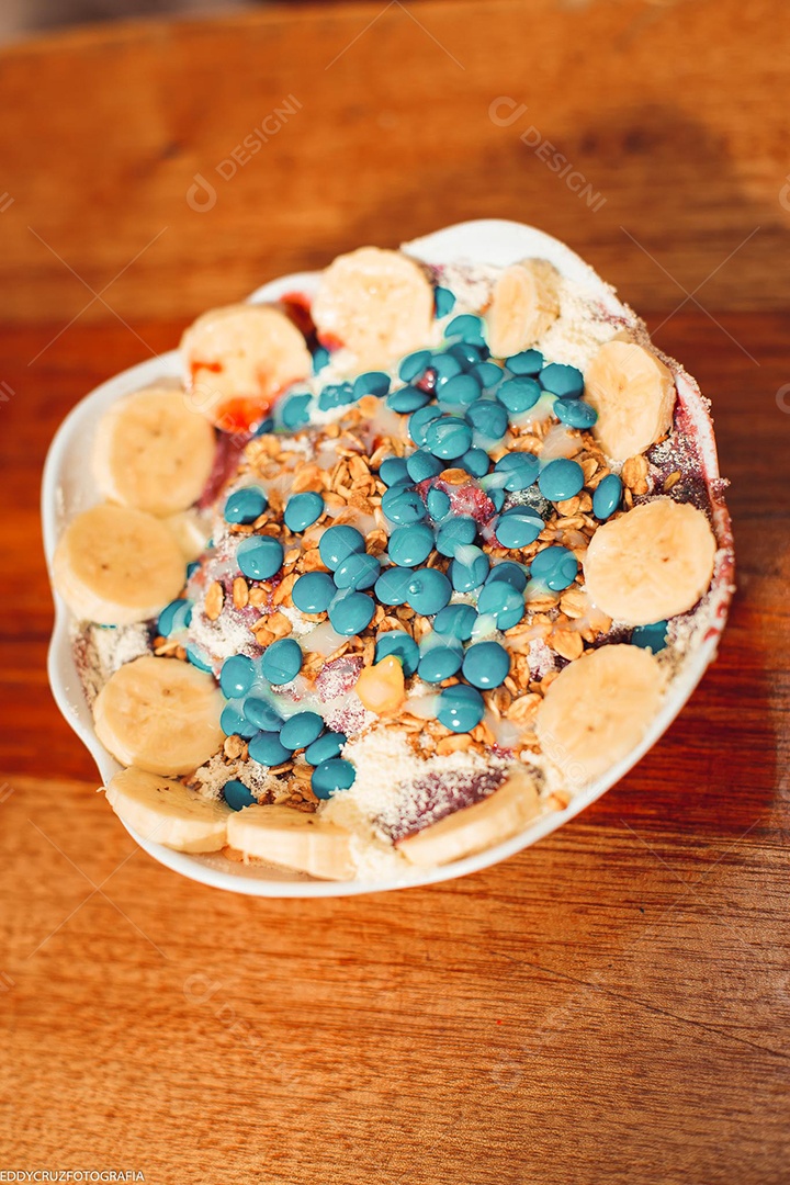 Tigela branca com Açaí com banana e acompanhamentos diversos.