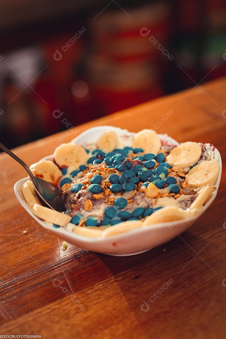 Tigela branca com Açaí com banana e acompanhamentos diversos.