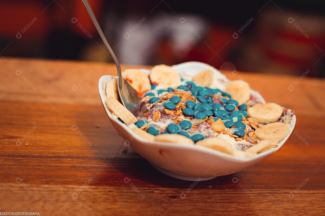 Tigela branca com Açaí com banana e acompanhamentos diversos.