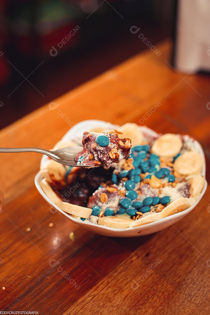 Tigela branca com Açaí com banana e acompanhamentos diversos.