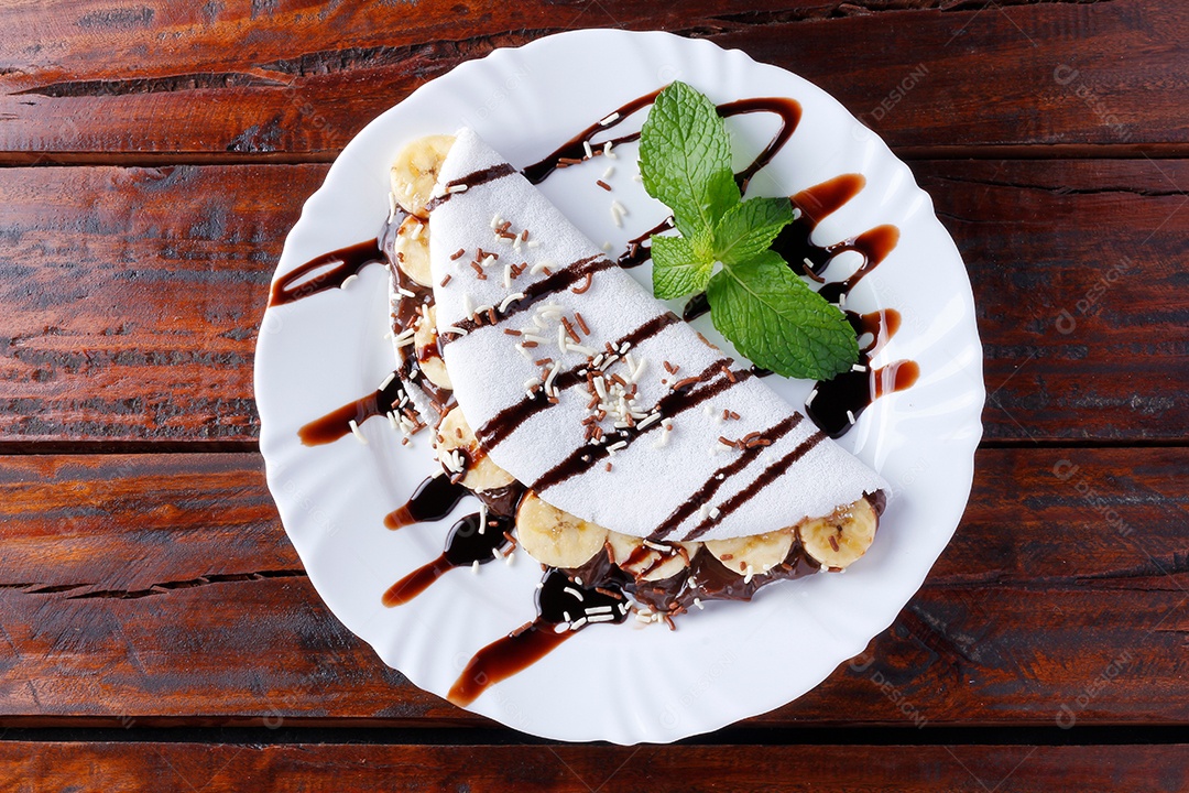 tapioca caseira ou beiju recheado com banana e chocolate na chapa branca sobre mesa de madeira rústica. vista do topo