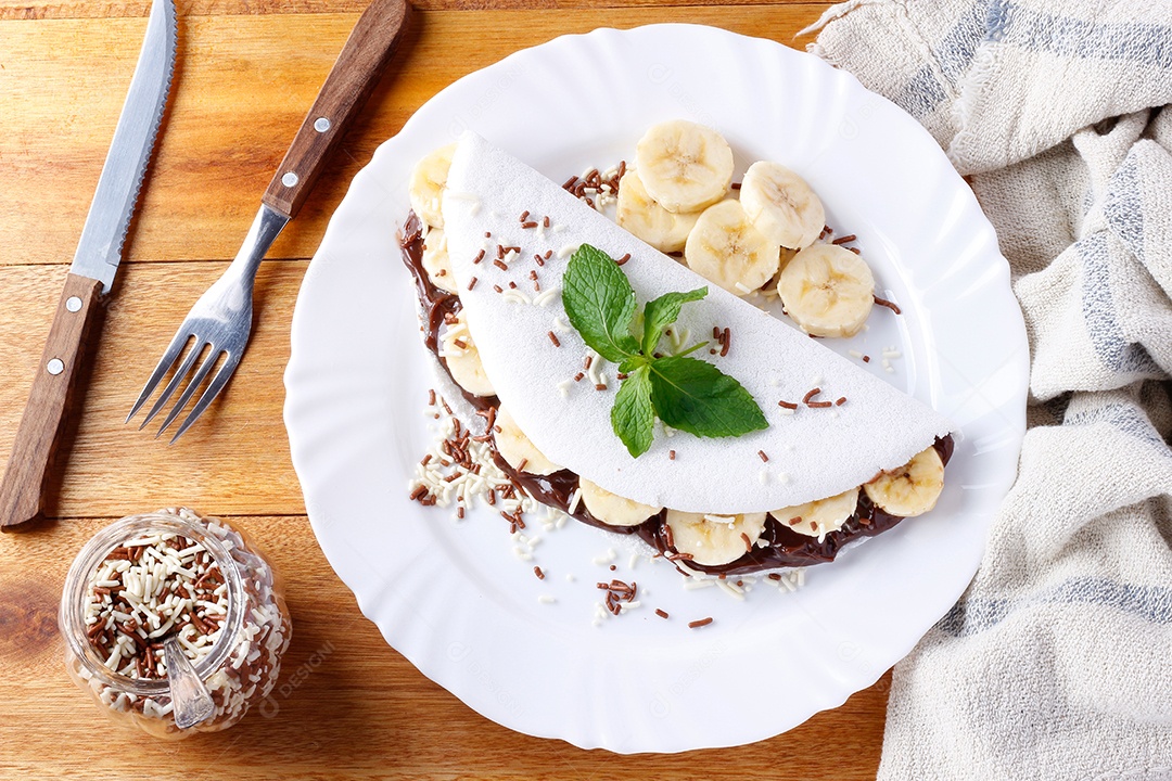 tapioca caseira ou beiju recheado com banana e chocolate na chapa branca sobre mesa de madeira rústica. vista do topo