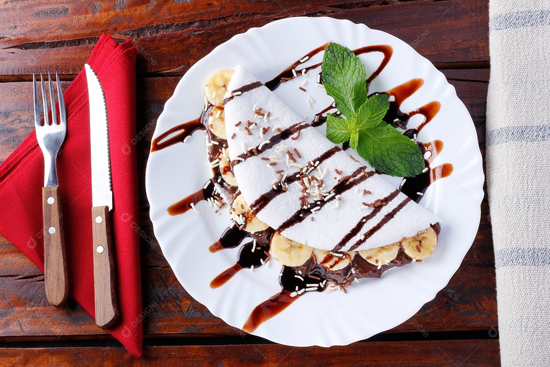 tapioca caseira ou beiju recheado com banana e chocolate na chapa branca sobre mesa de madeira rústica. vista do topo