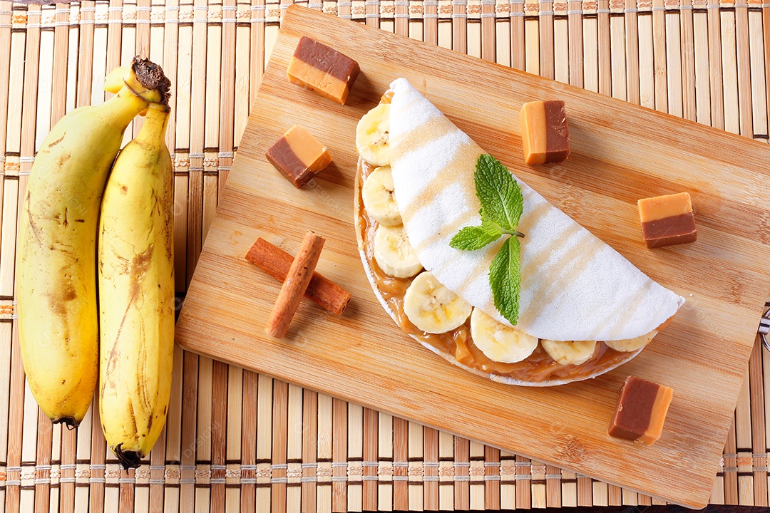 tapioca caseira ou beiju recheado com banana e leite condensado ou caramelo maltado na mesa de madeira rústica. vista do topo