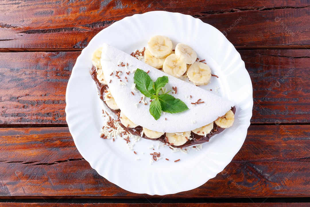 tapioca caseira ou beiju recheado com banana e chocolate na chapa branca sobre mesa de madeira rústica. vista do topo