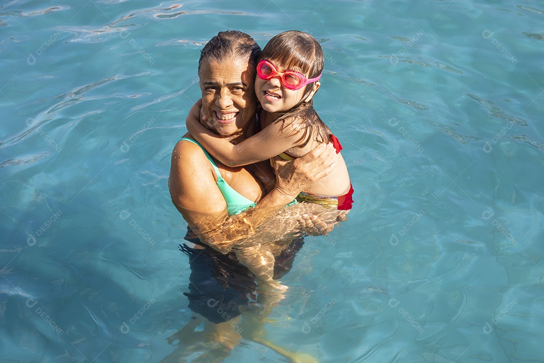 Família banhando e brincando na piscina de água azul.