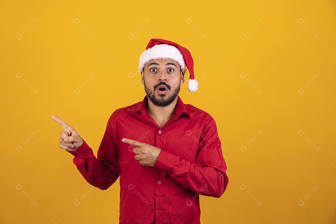 Homem bonito vestido para o natal com chapéu de papai Noel apontando promoção de fim de ano.
