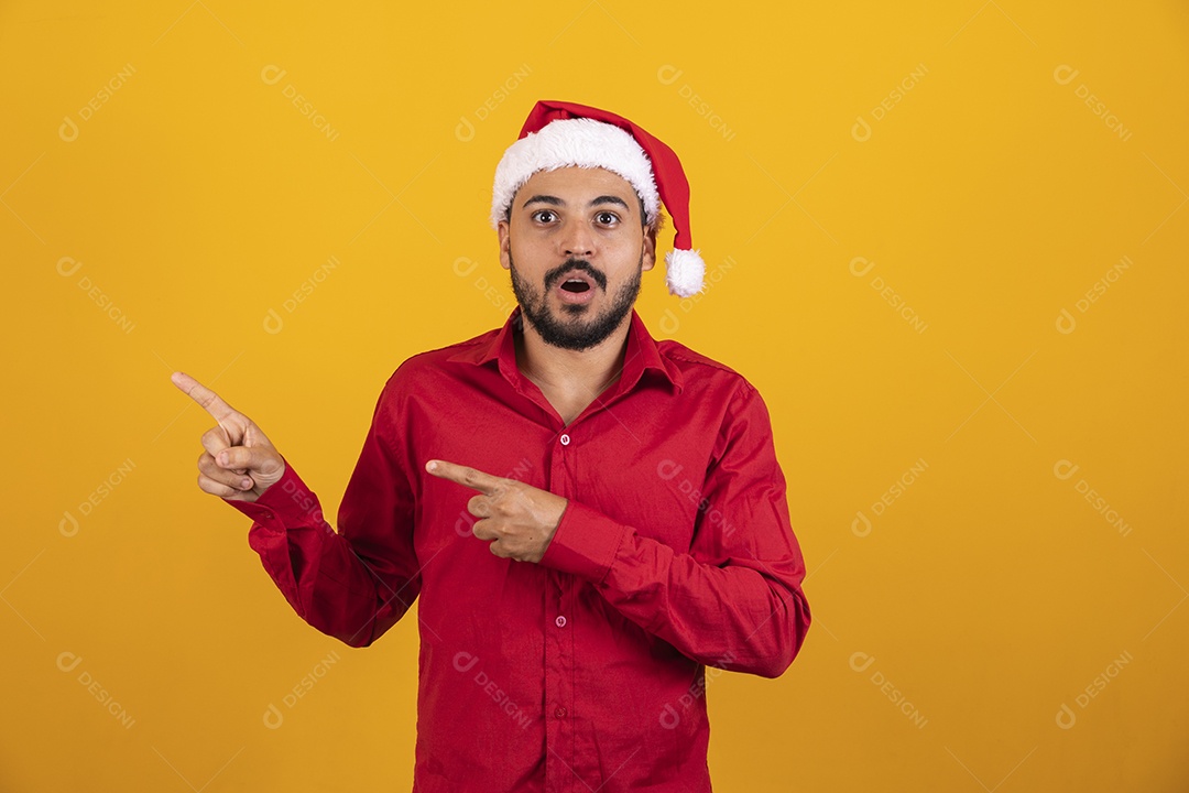 Homem bonito vestido para o natal com chapéu de papai Noel apontando promoção de fim de ano.