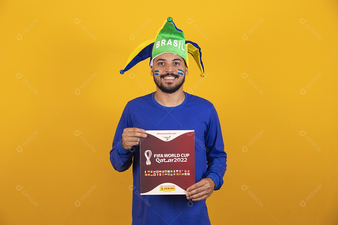 Homem brasileiro vestindo uma camiseta do Brasil e segurando um álbum da copa do mundo
