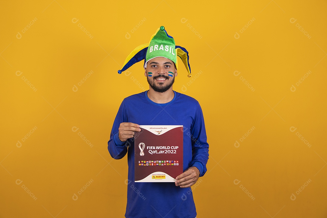 Homem brasileiro vestindo uma camiseta do Brasil e segurando um álbum da copa do mundo
