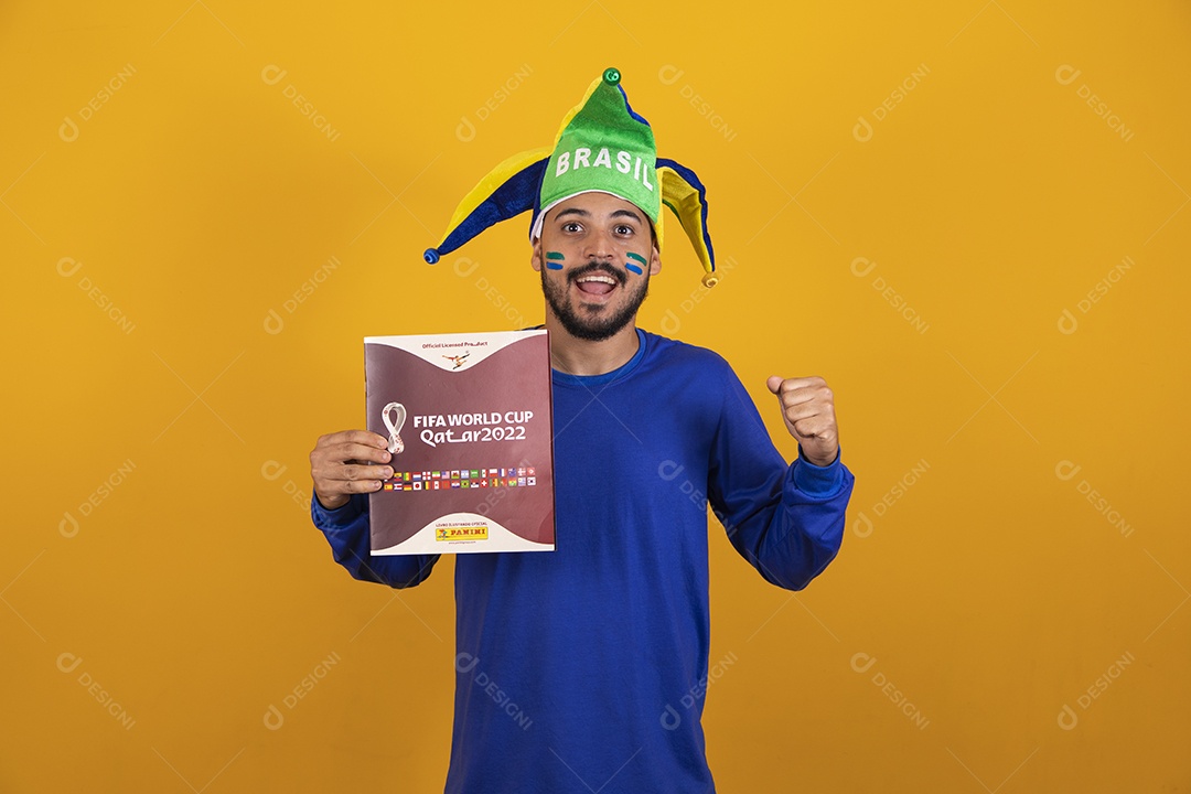 Homem brasileiro vestindo uma camiseta do Brasil e segurando um álbum da copa do mundo