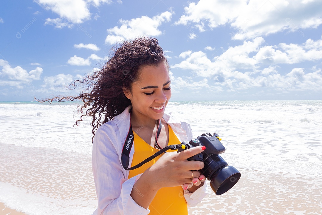 Mulher jovem segurando câmera fotográfica fotografando praia