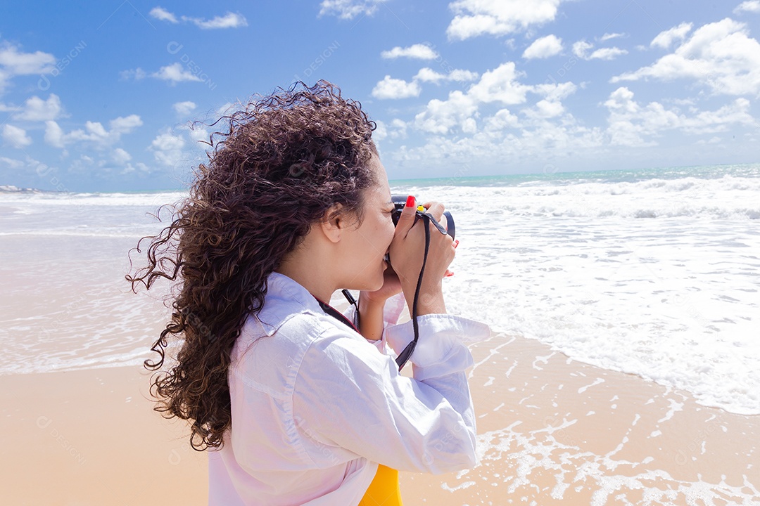 Mulher jovem segurando câmera fotográfica fotografando praia