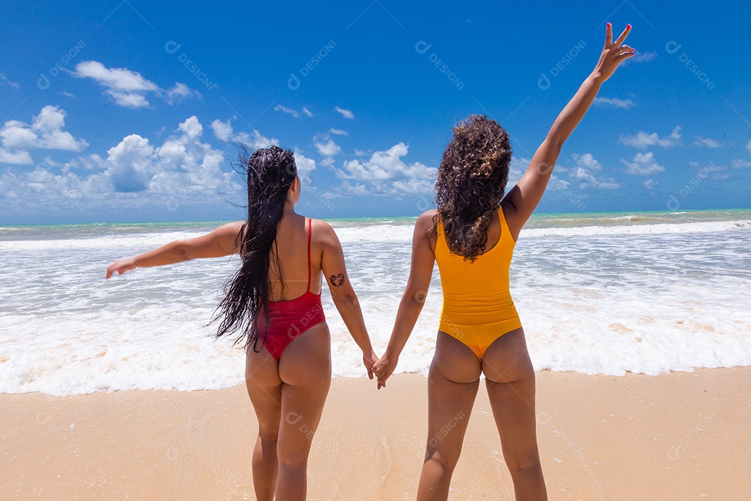 Lindas mulheres usando trajes de banho sobre praia curtindo verão