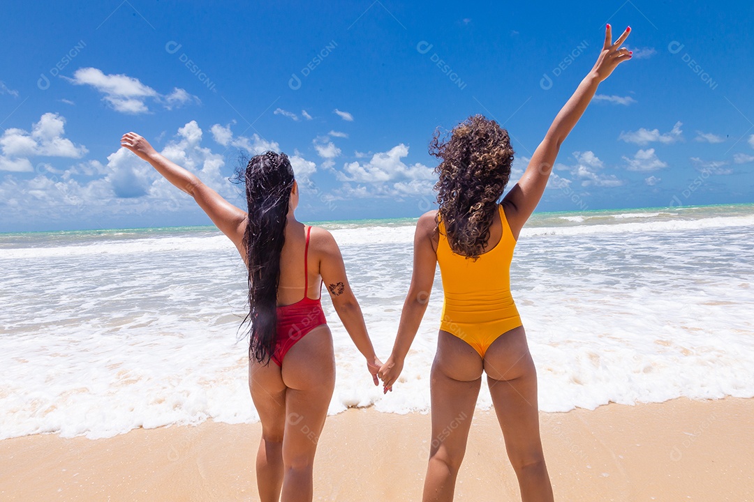 Lindas mulheres usando trajes de banho sobre praia curtindo verão