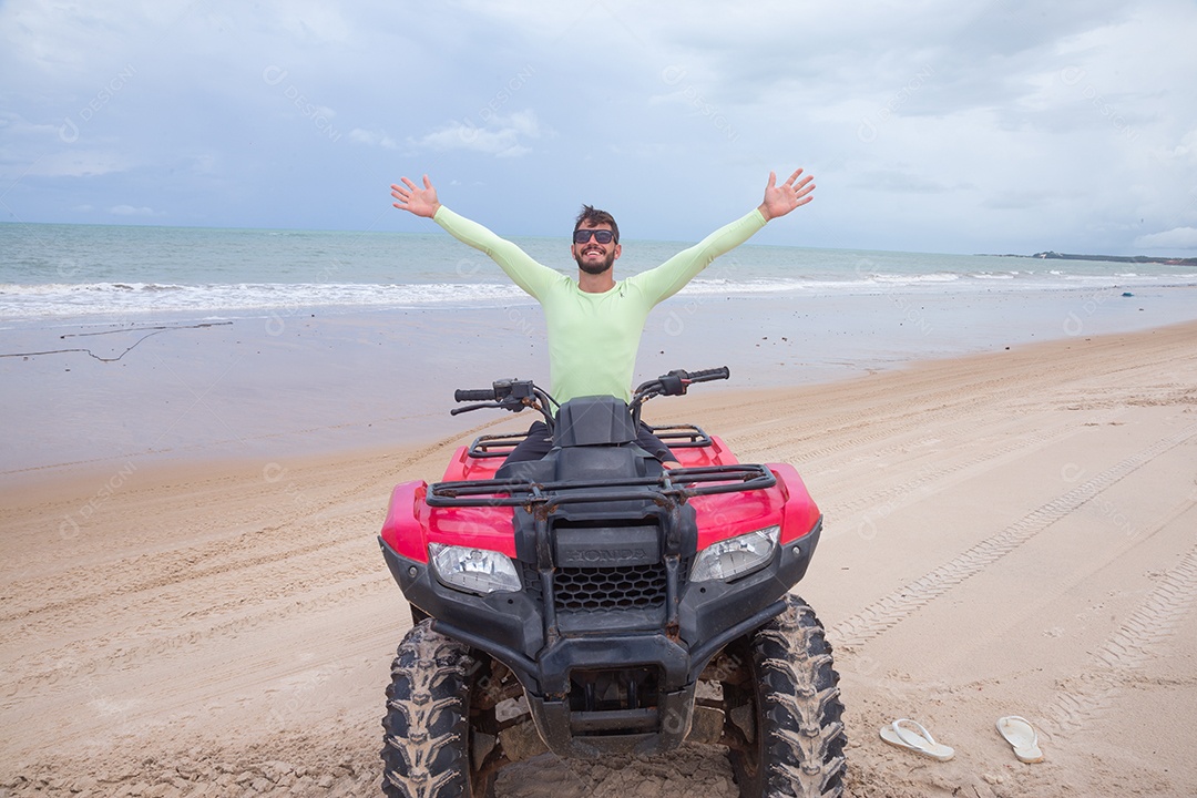 Homem jovem curtindo férias andando de quadriciclo sobre dunas